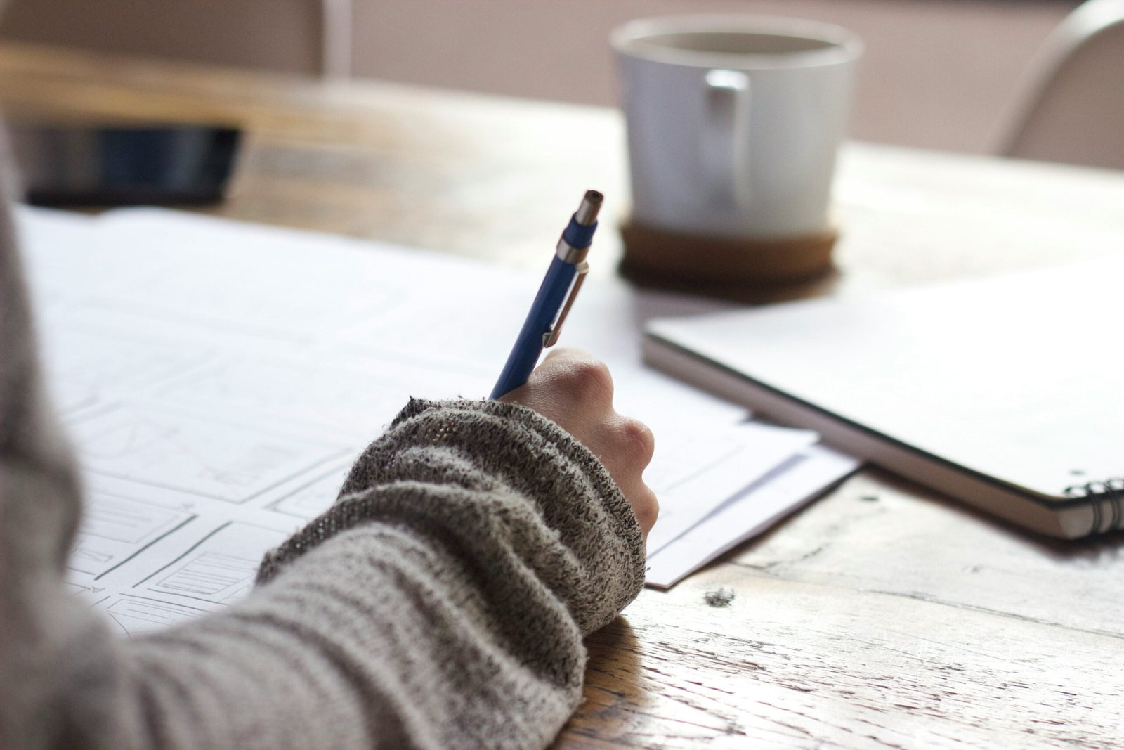 person writing on brown wooden table near white ceramic mug- essay writing tips